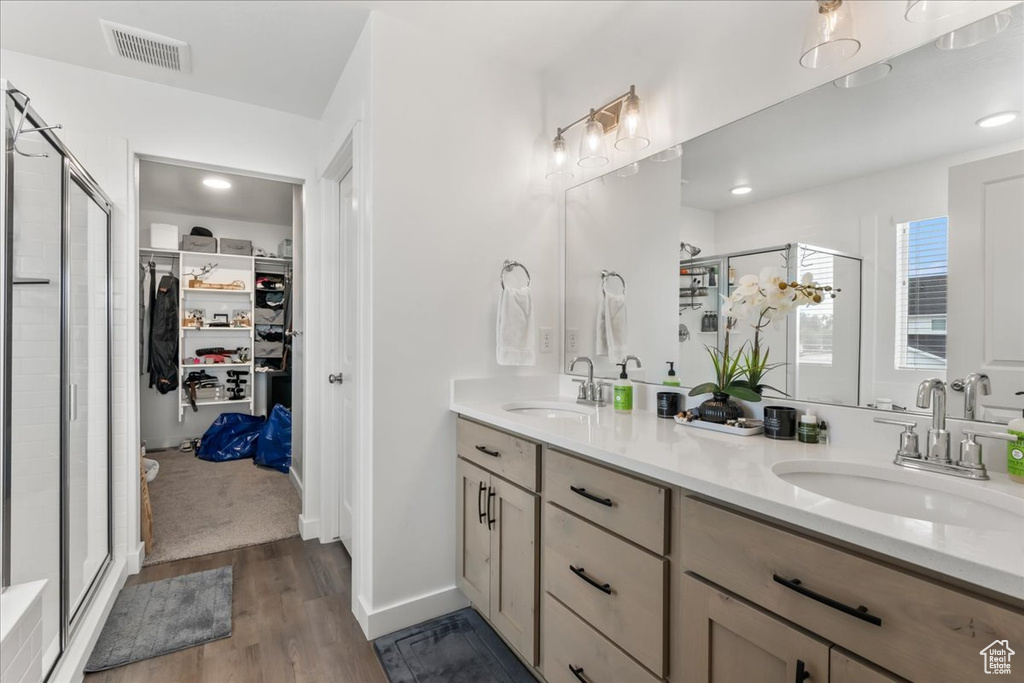 Bathroom featuring a walk in closet, double vanity, a stall shower, wood finished floors, and recessed lighting