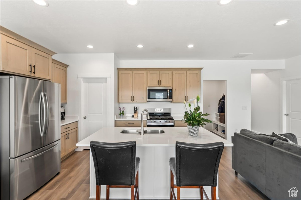 Kitchen with appliances with stainless steel finishes, a breakfast bar, light countertops, wood finished floors, and light brown cabinets