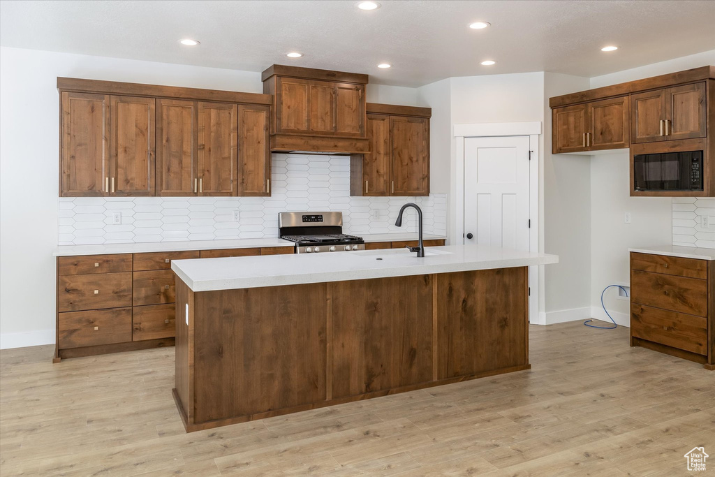 Kitchen featuring stainless steel range, black microwave, light countertops, premium range hood, and a center island with sink