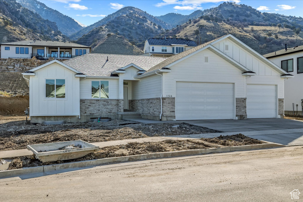 View of front facade with board and batten siding, an attached garage, driveway, a mountain view, and stone siding
