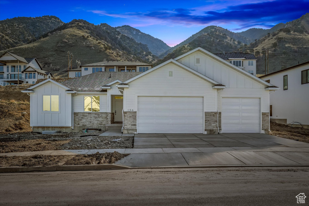View of front of home featuring board and batten siding, an attached garage, driveway, a mountain view, and stone siding