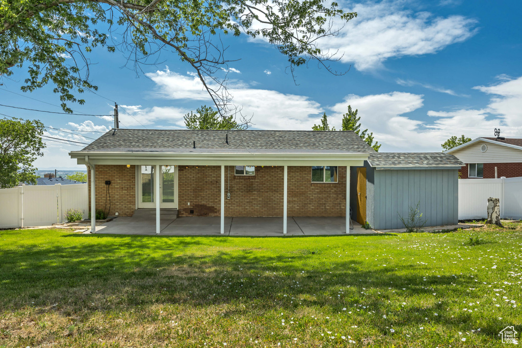 Back of house with a fenced backyard, a patio area, brick siding, a shingled roof, and a shed