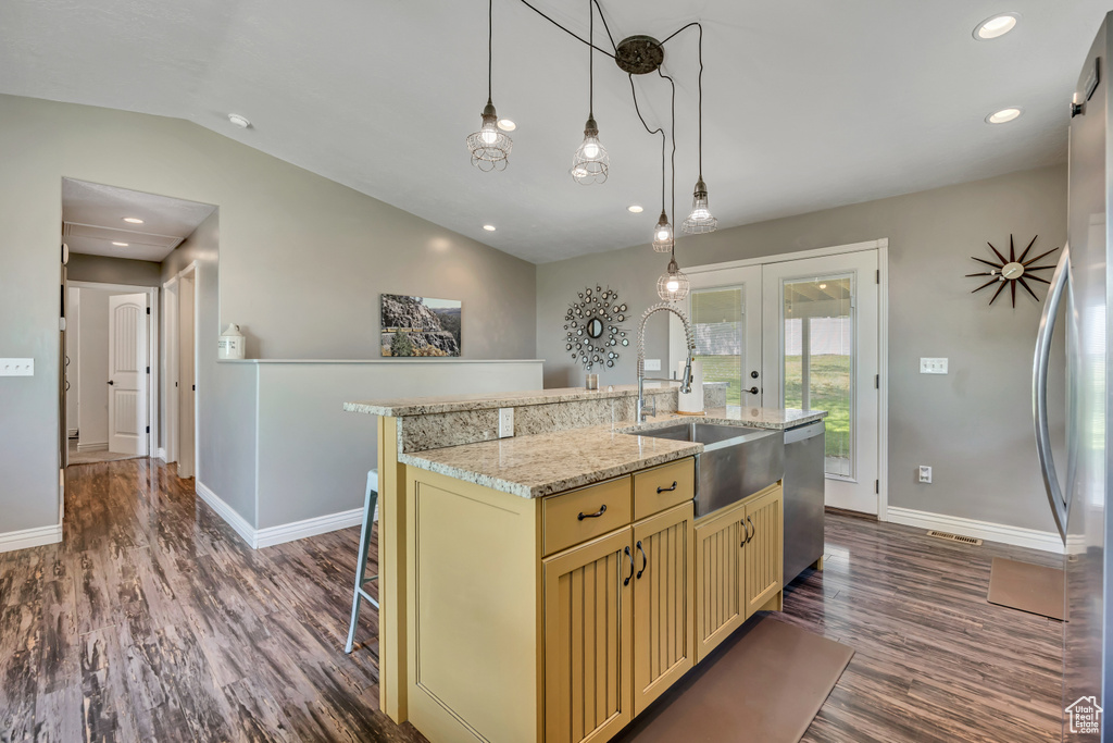Kitchen with stainless steel appliances, cream cabinets, dark wood finished floors, vaulted ceiling, and a kitchen island with sink