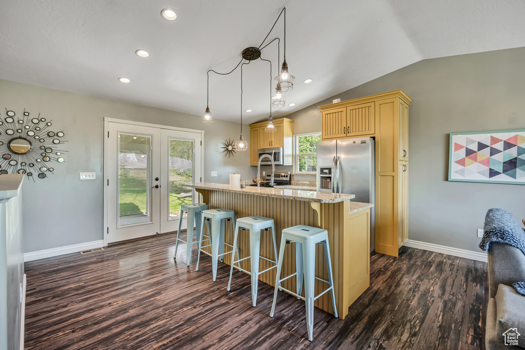 Kitchen featuring appliances with stainless steel finishes, dark wood-style flooring, a kitchen bar, vaulted ceiling, and a kitchen island with sink