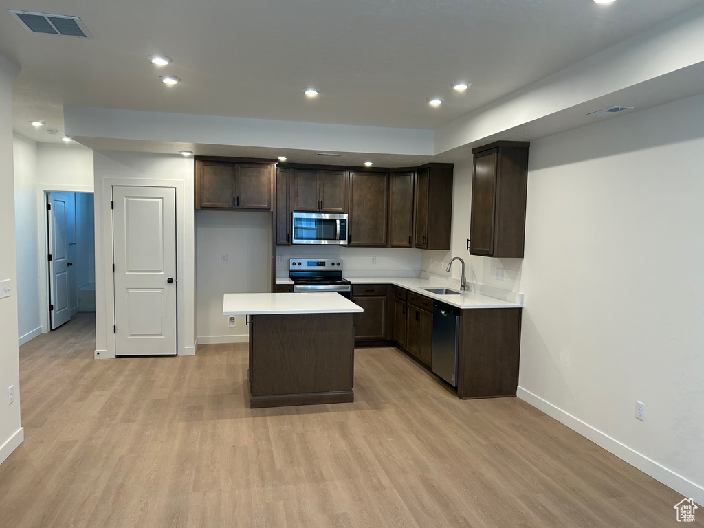 Kitchen featuring stainless steel appliances, light wood-style floors, dark brown cabinets, light countertops, and a kitchen island