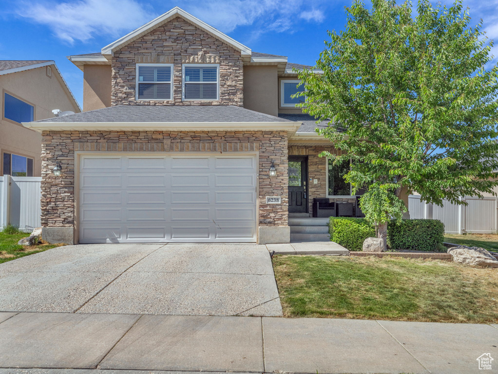 View of front facade with concrete driveway, stone siding, a garage, and stucco siding
