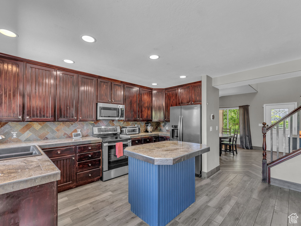 Kitchen with appliances with stainless steel finishes, recessed lighting, backsplash, light wood finished floors, and a center island