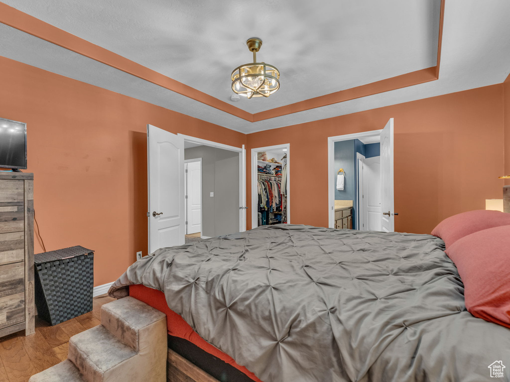 Bedroom featuring wood finished floors, a chandelier, a raised ceiling, and a spacious closet