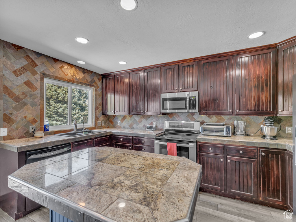 Kitchen featuring appliances with stainless steel finishes, recessed lighting, tasteful backsplash, light wood-type flooring, and a kitchen island