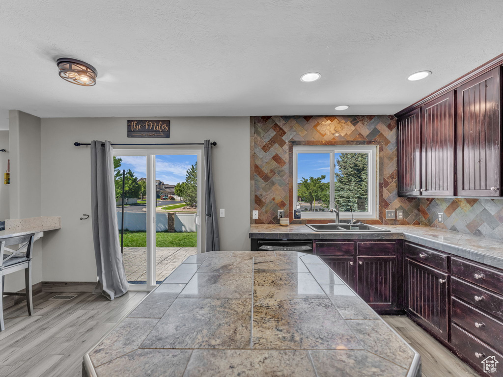 Kitchen with tasteful backsplash, tile counters, light wood finished floors, reddish brown cabinets, and recessed lighting
