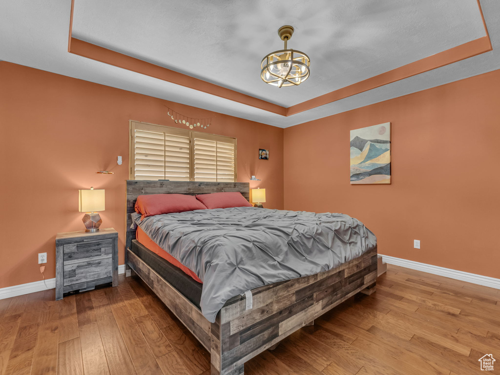 Bedroom featuring a tray ceiling, a chandelier, and hardwood / wood-style flooring