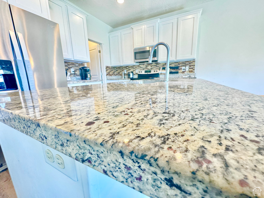 Kitchen featuring appliances with stainless steel finishes, decorative backsplash, white cabinets, and light stone countertops