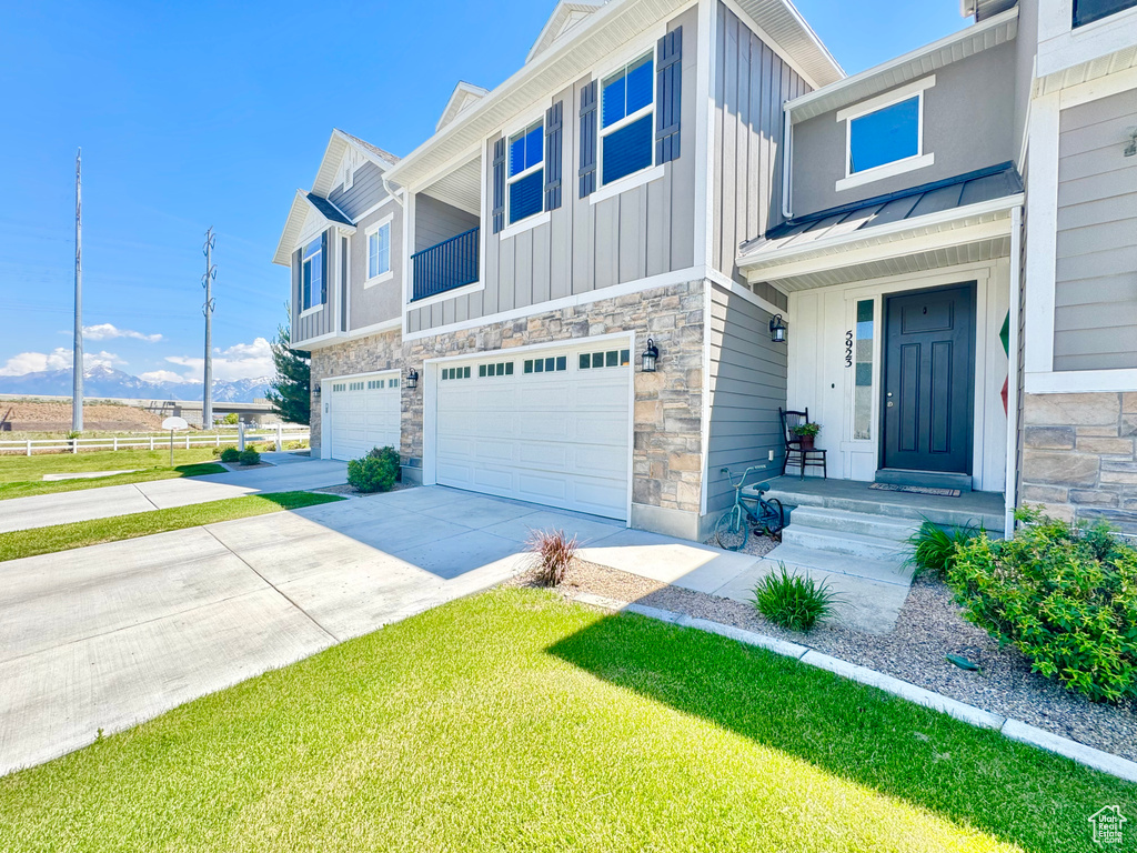 View of front of home with an attached garage, board and batten siding, stone siding, driveway, and a metal roof