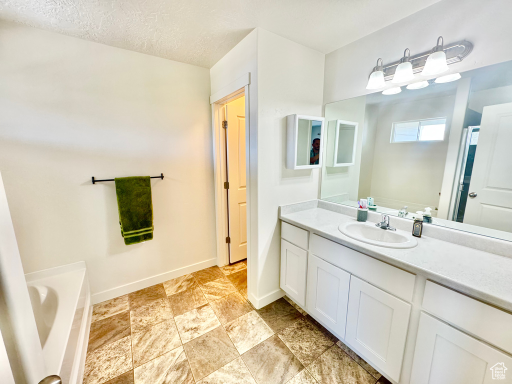 Bathroom featuring vanity, a garden tub, stone finish flooring, and a textured ceiling