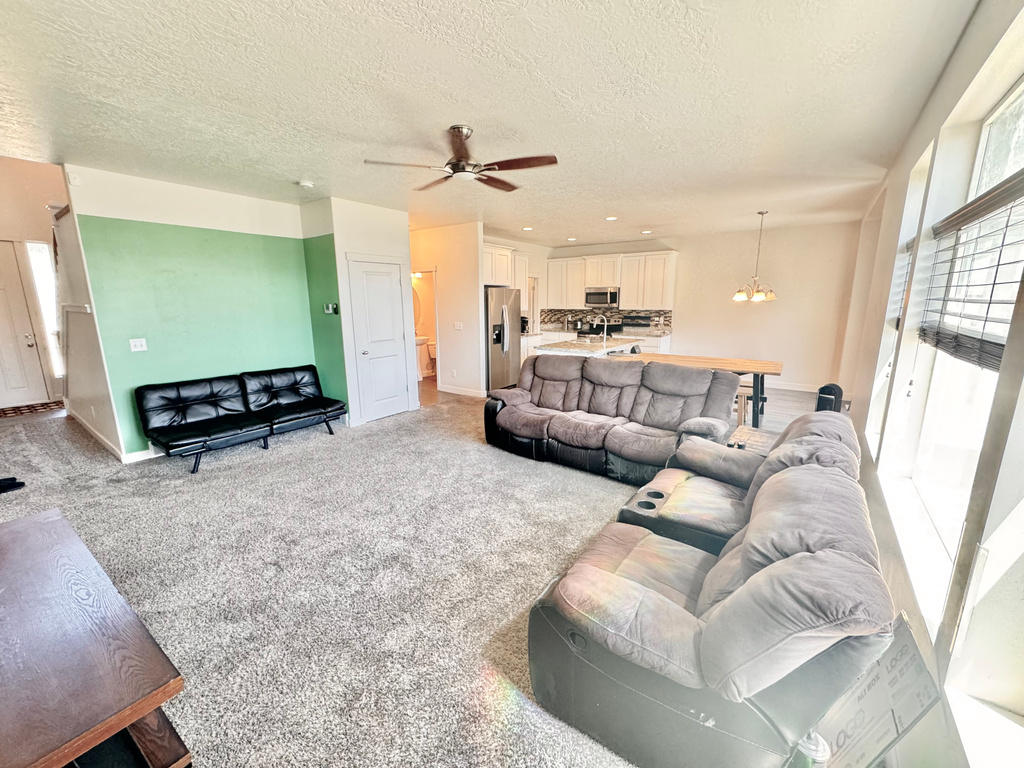 Living room featuring a textured ceiling, light carpet, a ceiling fan, and a chandelier