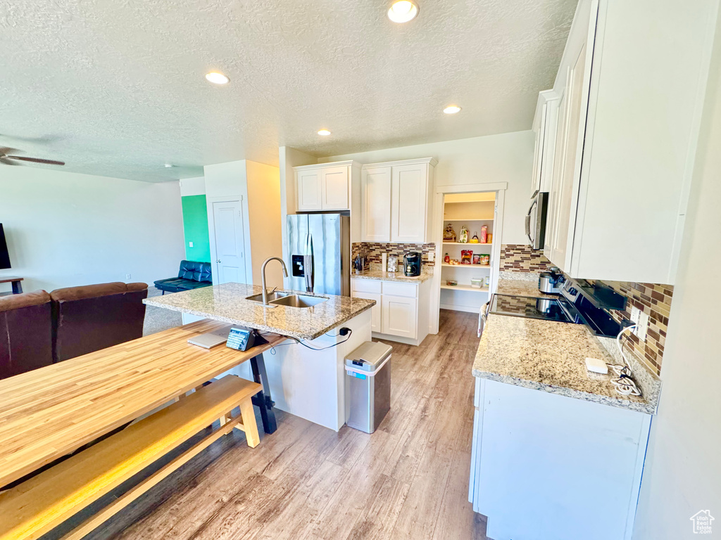 Kitchen featuring appliances with stainless steel finishes, open floor plan, a textured ceiling, white cabinets, and light wood-style flooring