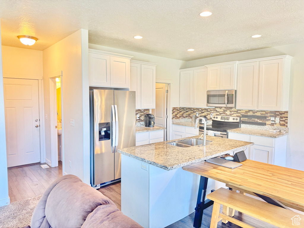 Kitchen with stainless steel appliances, backsplash, white cabinetry, an island with sink, and a textured ceiling