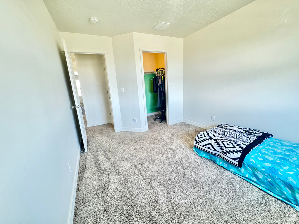 Unfurnished bedroom featuring carpet floors, a textured ceiling, a spacious closet, and a closet