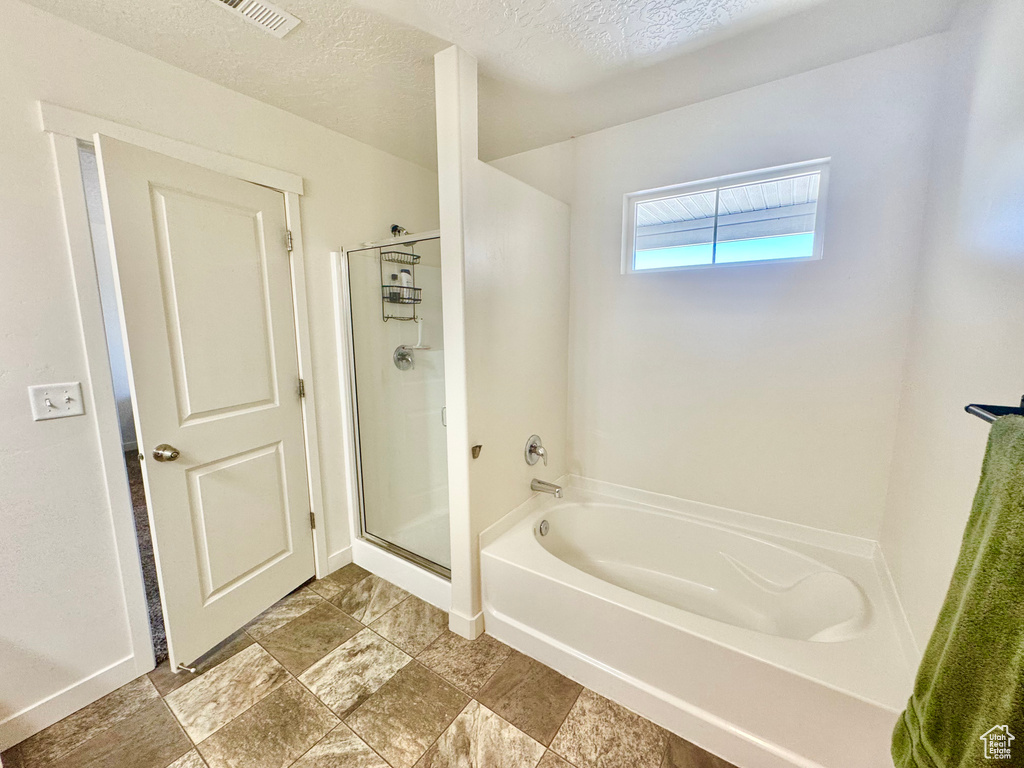 Bathroom featuring a garden tub, a shower stall, and a textured ceiling