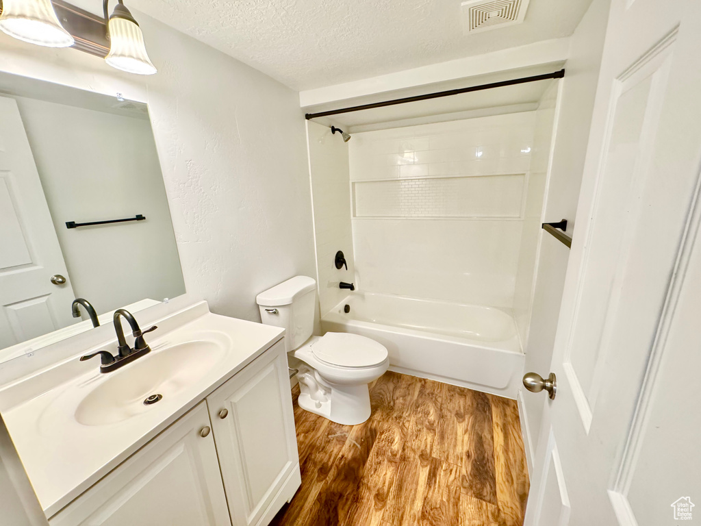 Full bathroom featuring a textured ceiling, wood finished floors, vanity, and  shower combination