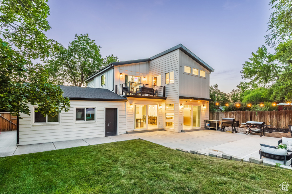 Back of house at dusk with a balcony and a patio area