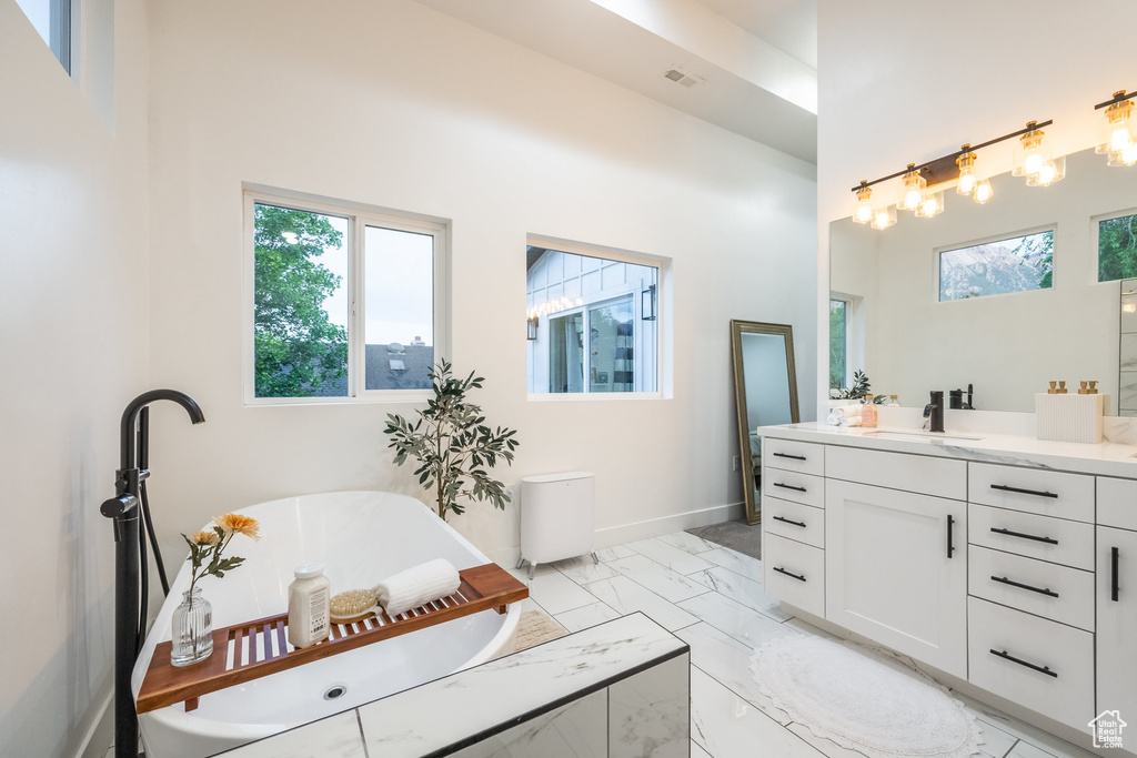 Full bathroom featuring vanity, a freestanding tub, marble look tile flooring, and a high ceiling