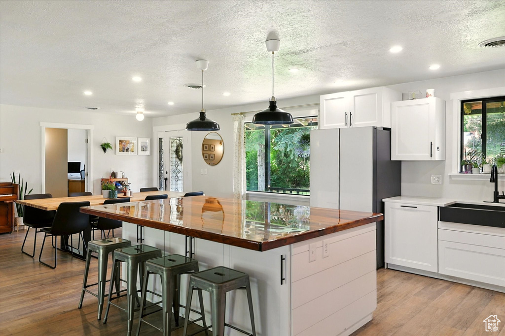 Kitchen with butcher block countertops, recessed lighting, a textured ceiling, wood finished floors, and white cabinets