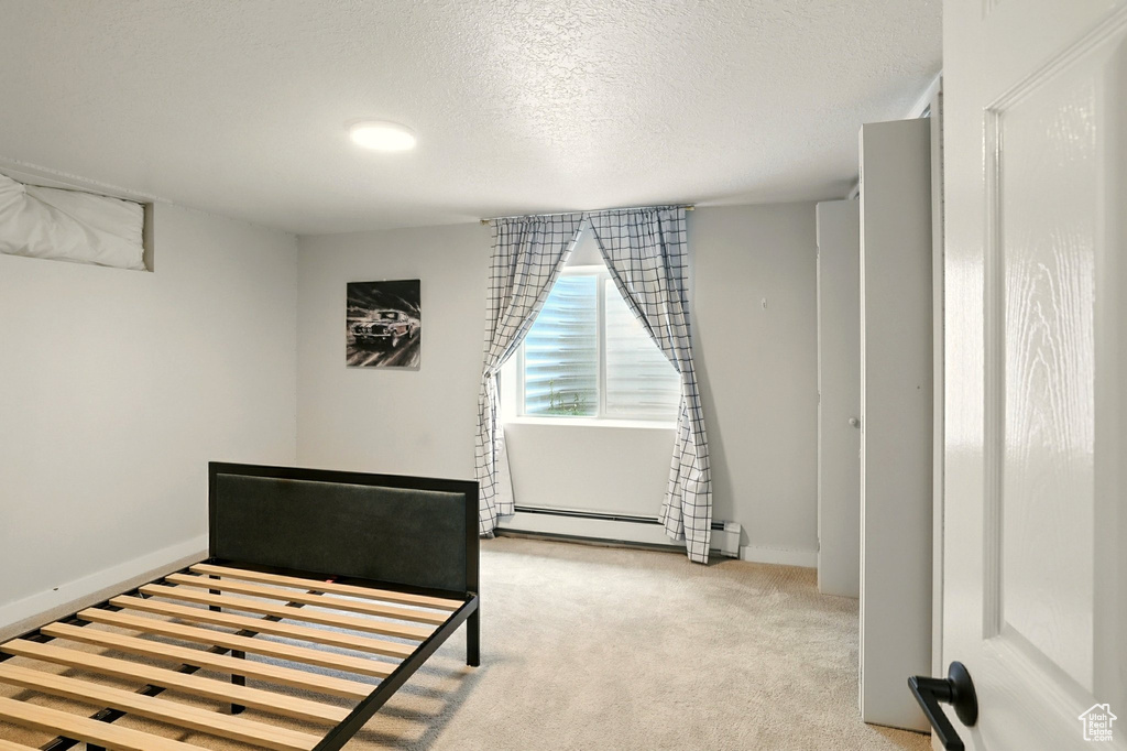 Bedroom featuring baseboard heating, a textured ceiling, and light colored carpet