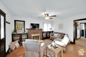Living room featuring ceiling fan, a brick fireplace, and wood finished floors