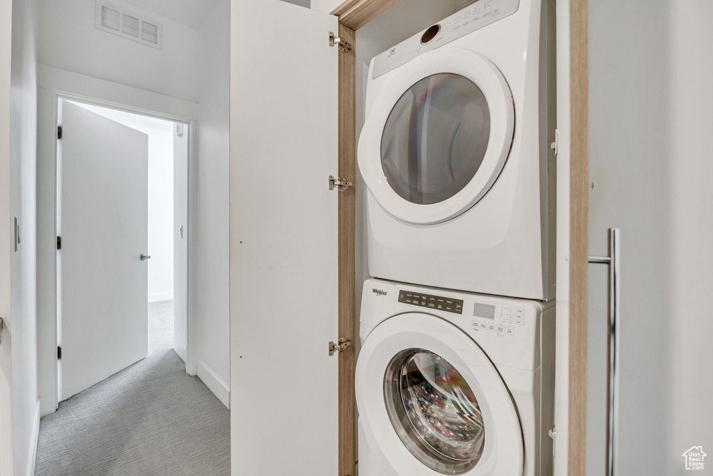 Laundry room featuring stacked washer / dryer and light carpet