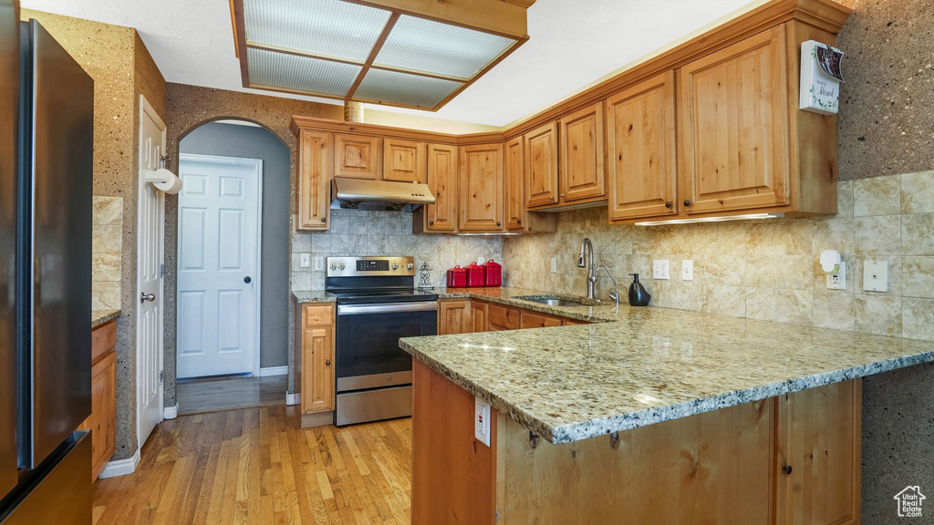 Kitchen with stainless steel appliances, under cabinet range hood, light wood-style flooring, light stone countertops, and a peninsula