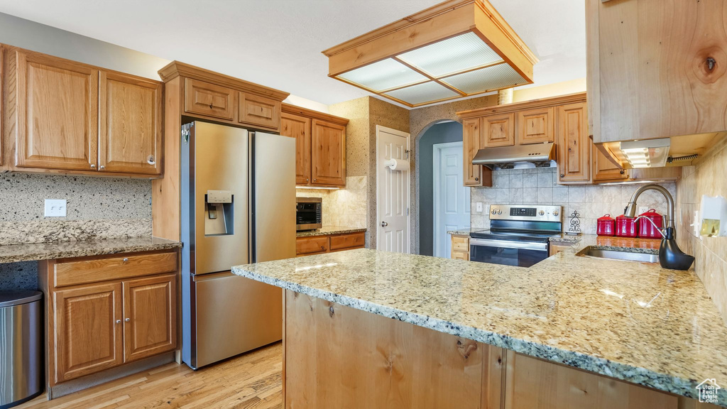 Kitchen with appliances with stainless steel finishes, under cabinet range hood, light stone countertops, and decorative backsplash