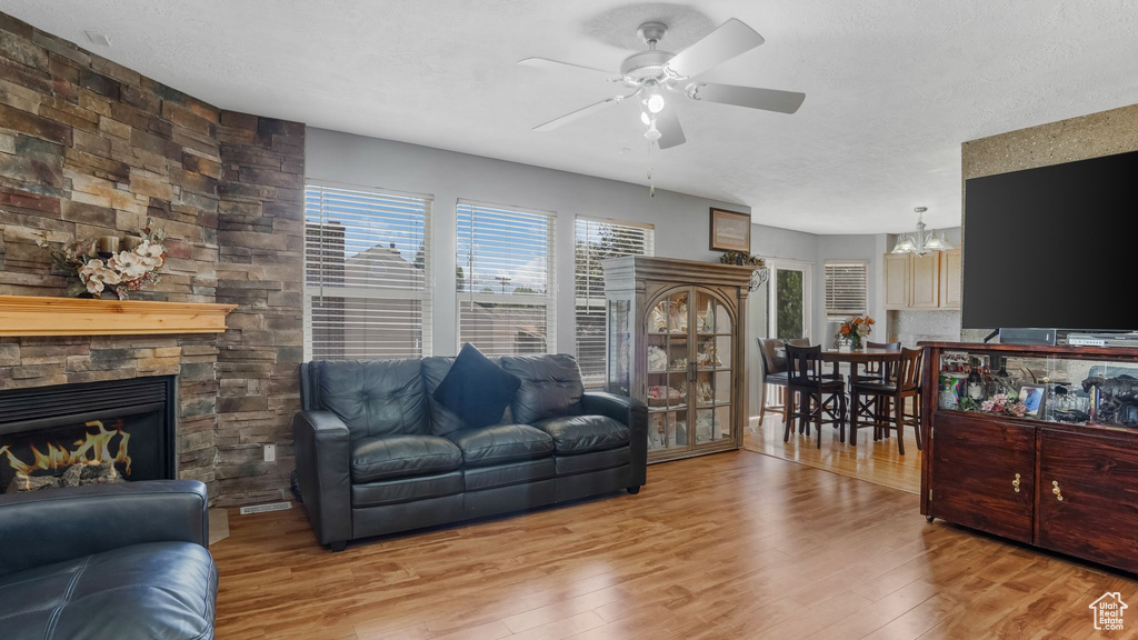 Living room with ceiling fan, wood finished floors, a fireplace, and a chandelier