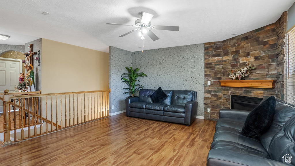 Living area featuring ceiling fan, wood finished floors, and a stone fireplace
