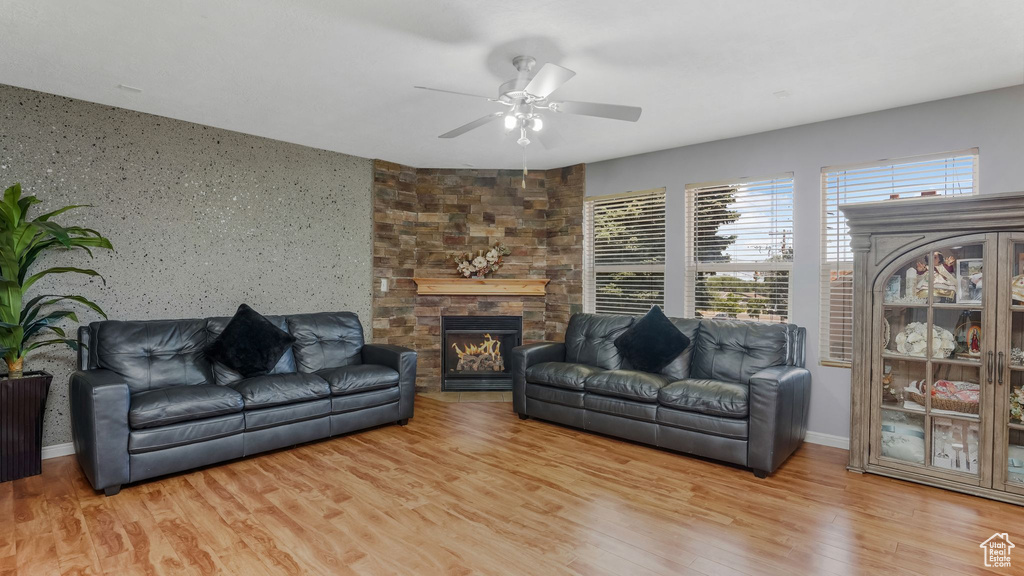 Living room with ceiling fan, wood finished floors, healthy amount of natural light, and a stone fireplace