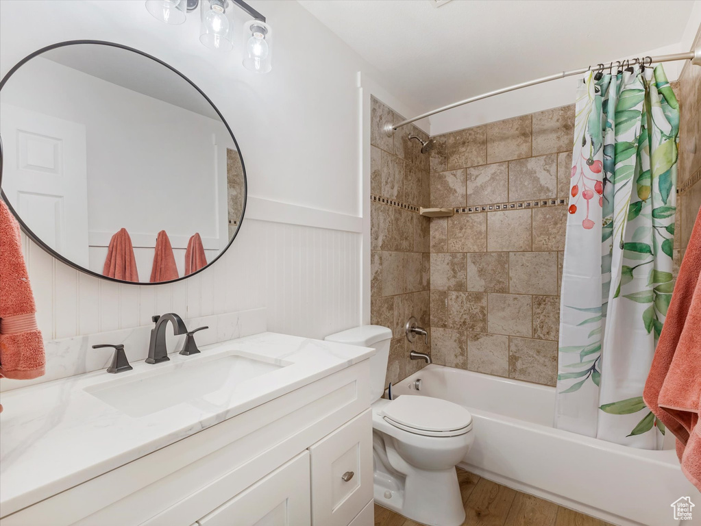 Full bath with shower / tub combo, vanity, wood finished floors, and a wainscoted wall