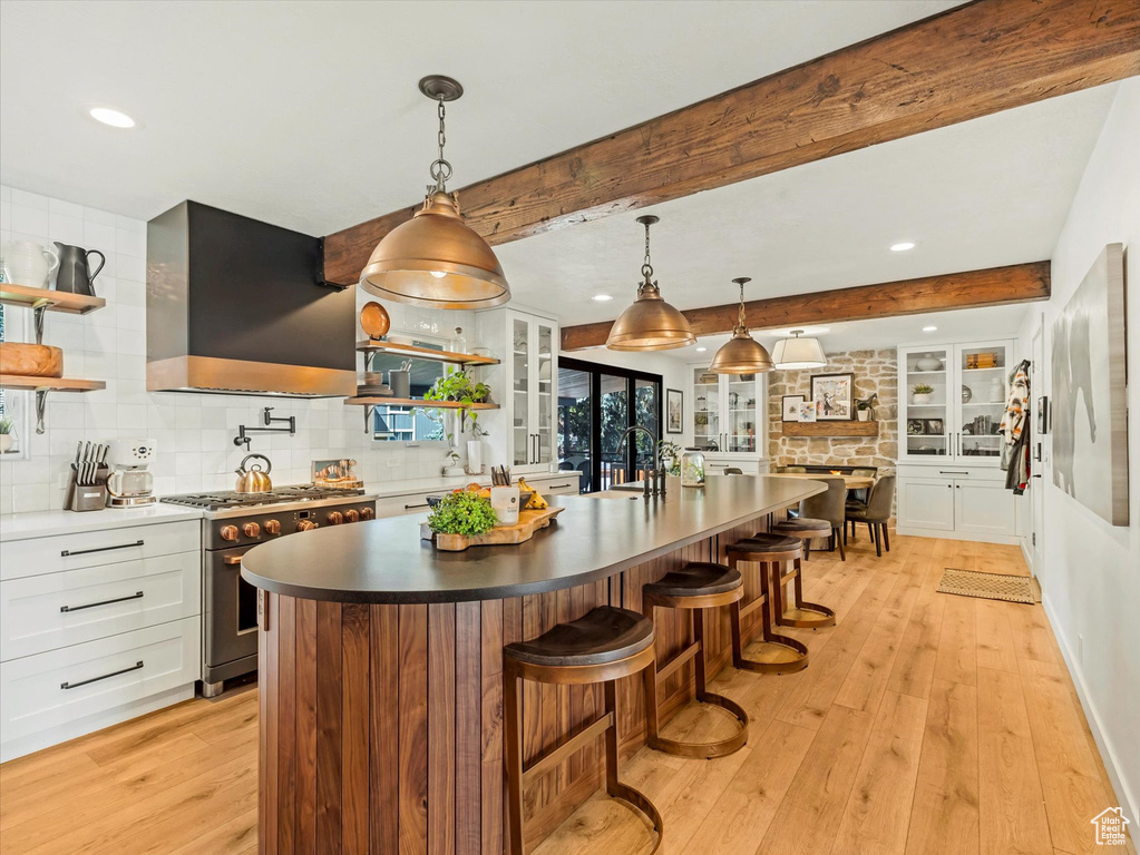 Kitchen featuring stainless steel range with gas cooktop, extractor fan, open shelves, light wood finished floors, and beamed ceiling