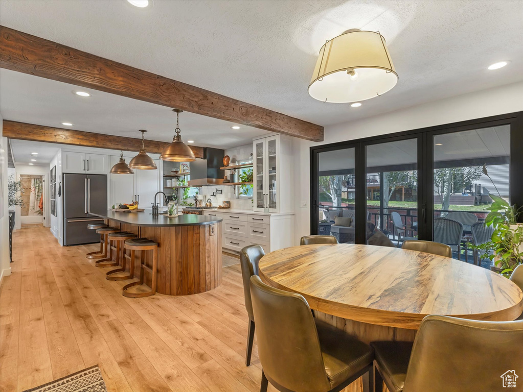Dining space featuring beamed ceiling, light wood-style floors, recessed lighting, and a textured ceiling