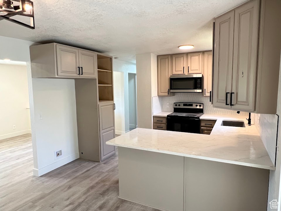 Kitchen featuring electric stove, stainless steel microwave, a peninsula, light stone countertops, and light wood-type flooring