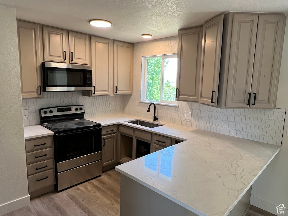 Kitchen with appliances with stainless steel finishes, a peninsula, gray cabinets, light wood-style floors, and backsplash