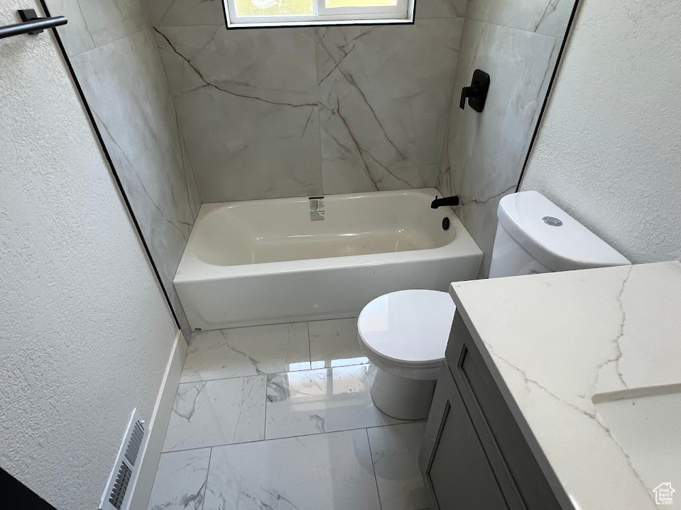 Bathroom featuring marble finish flooring, a textured wall, vanity, and  shower combination