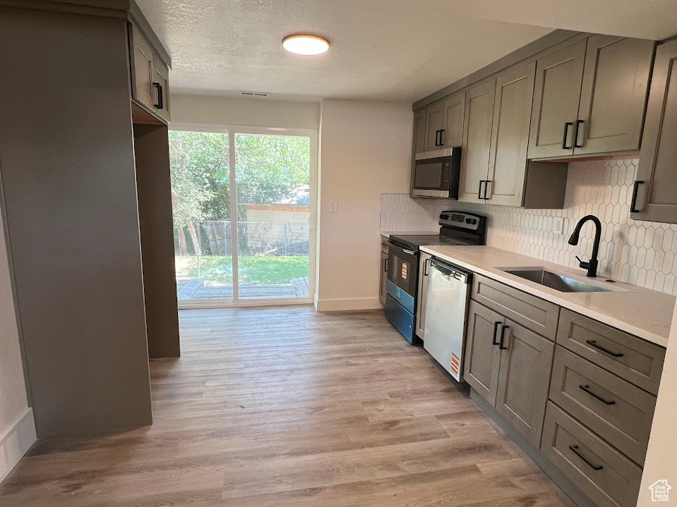 Kitchen with stainless steel appliances, decorative backsplash, light wood-type flooring, light countertops, and a textured ceiling