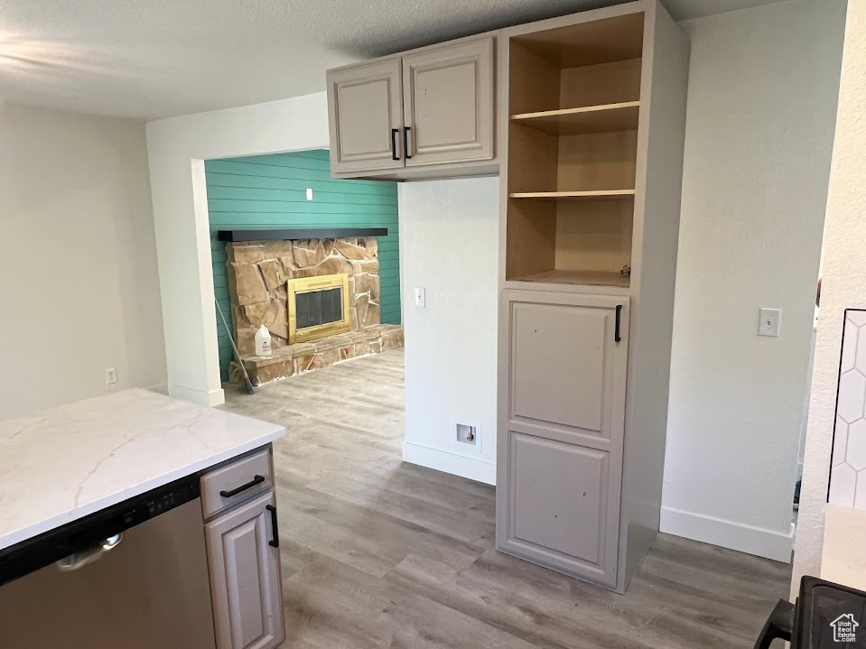 Kitchen with stainless steel dishwasher, wood finished floors, light stone countertops, and a fireplace