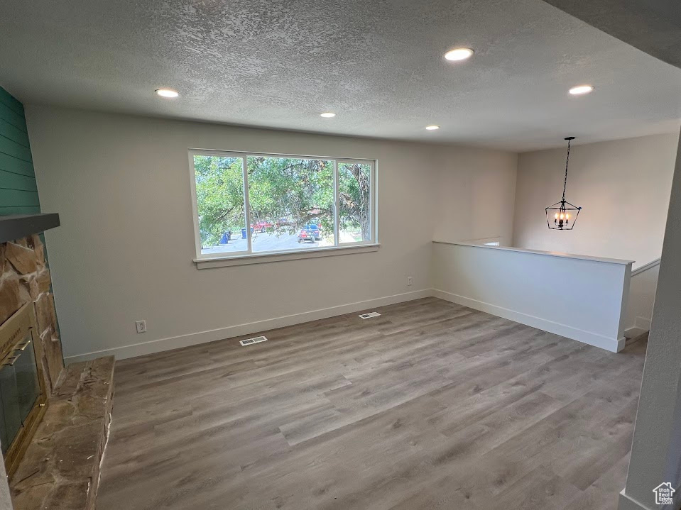 Unfurnished living room with a fireplace, recessed lighting, a textured ceiling, wood finished floors, and a chandelier