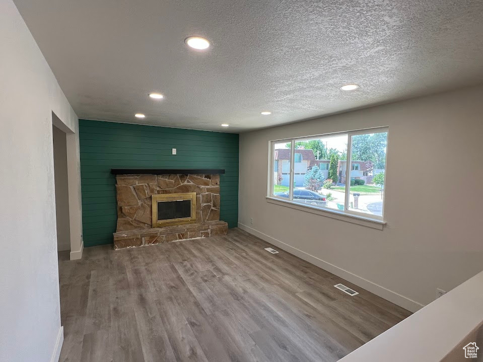 Unfurnished living room featuring recessed lighting, wood finished floors, a textured ceiling, a stone fireplace, and an accent wall