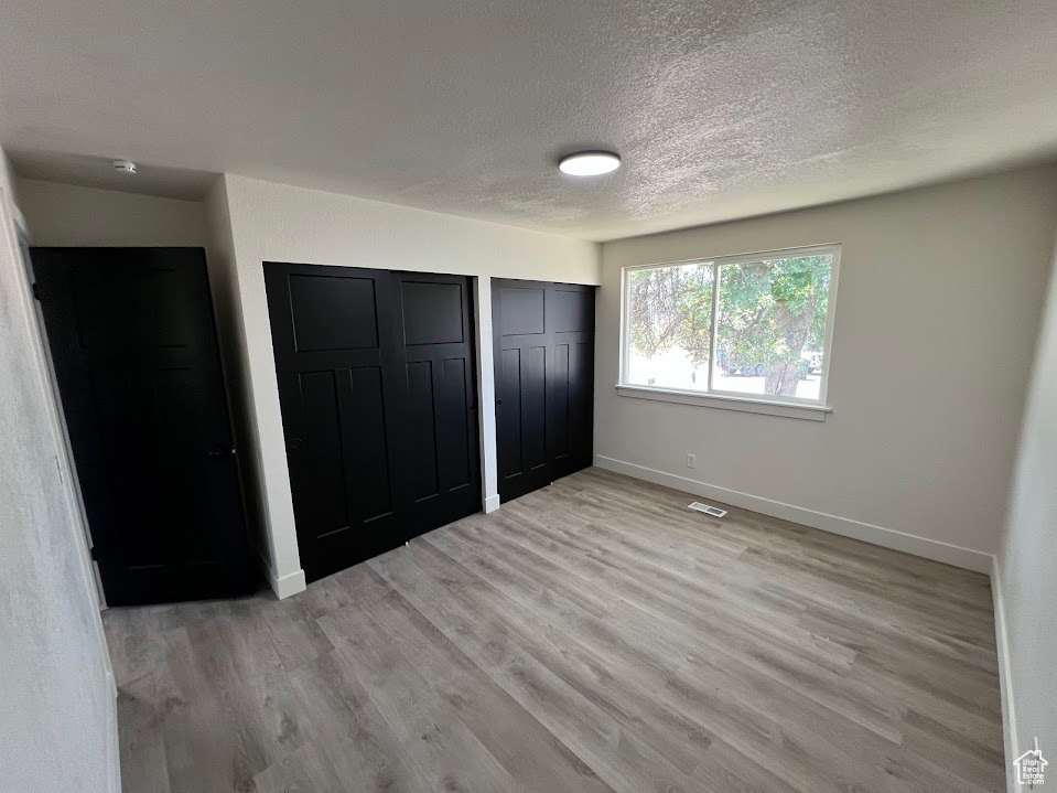 Unfurnished bedroom with a textured ceiling, multiple closets, and light wood-style flooring