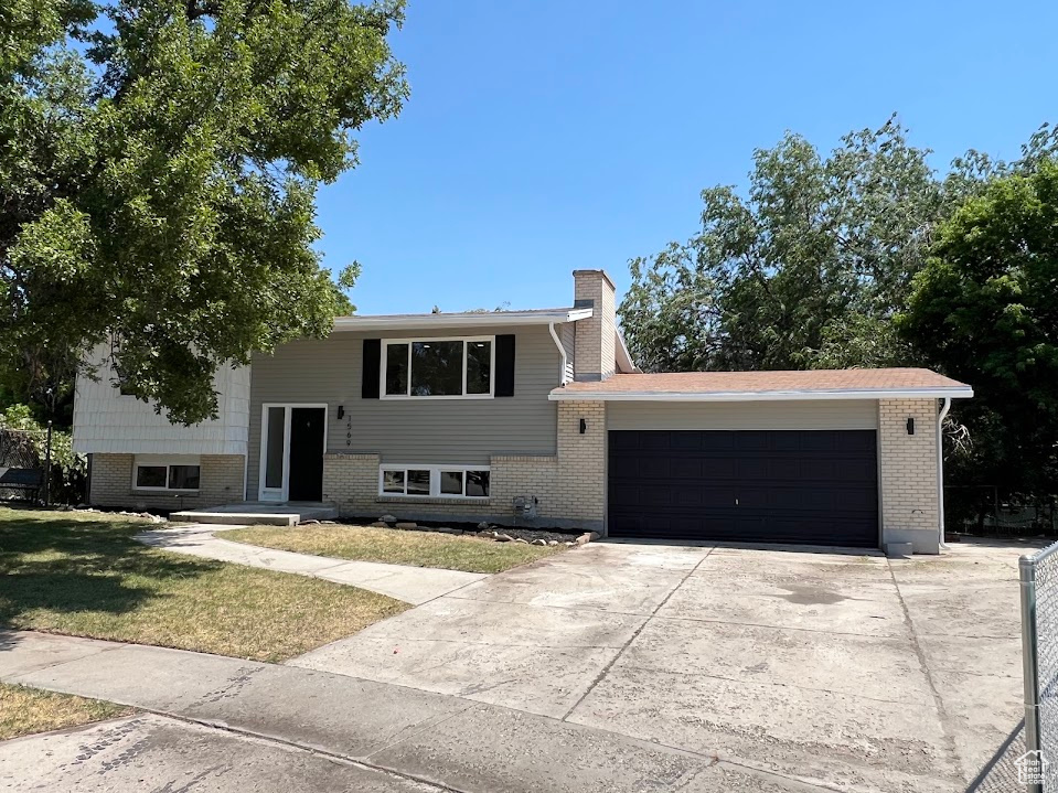 Split foyer home with a garage, a chimney, concrete driveway, brick siding, and a front lawn
