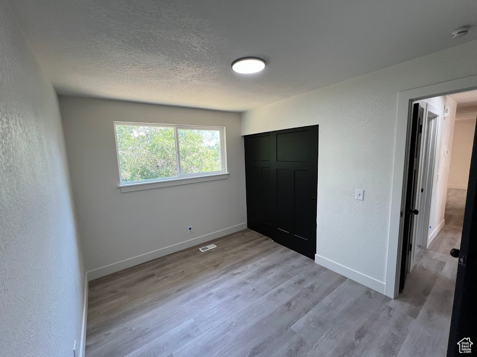 Unfurnished bedroom with light wood-type flooring, a textured wall, a textured ceiling, and a closet