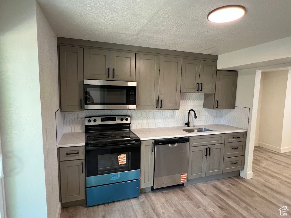 Kitchen featuring appliances with stainless steel finishes, gray cabinetry, tasteful backsplash, light wood-style floors, and a textured ceiling