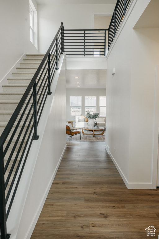 Hall with healthy amount of natural light, wood finished floors, stairway, and a high ceiling